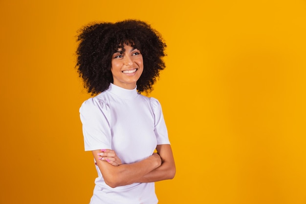 Ritratto di bella donna afro sorridente in piedi con le braccia incrociate. Sfondo giallo