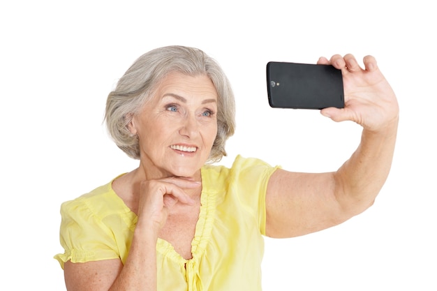 Ritratto di bella donna anziana che prende la foto del selfie su fondo bianco