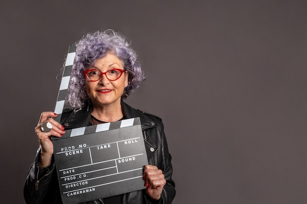 Ritratto di bella donna anziana che tiene un batacchio di film su uno spazio grigio