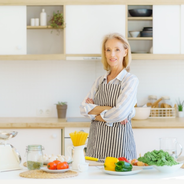 Ritratto di bella donna anziana in piedi in cucina e sorridente