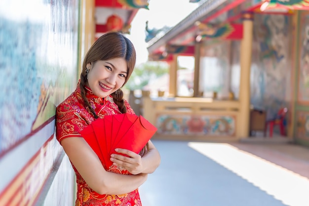 Ritratto di bella donna asiatica in abito Cheongsam con busta rossa in manoPopolo tailandeseFelice concetto di nuovo anno cinese