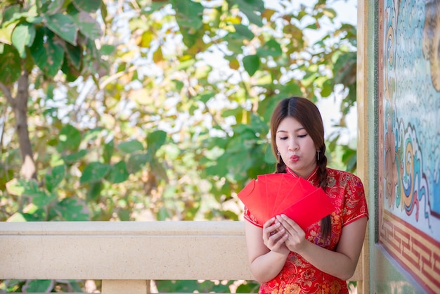 Ritratto di bella donna asiatica in abito Cheongsam con busta rossa in manoPopolo tailandeseFelice concetto di nuovo anno cinese