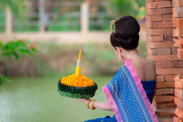 Ritratto di bella donna asiatica in abito tailandese tradizionale pregando tenere kratong per unirsi al festival loy kratong in thailandia