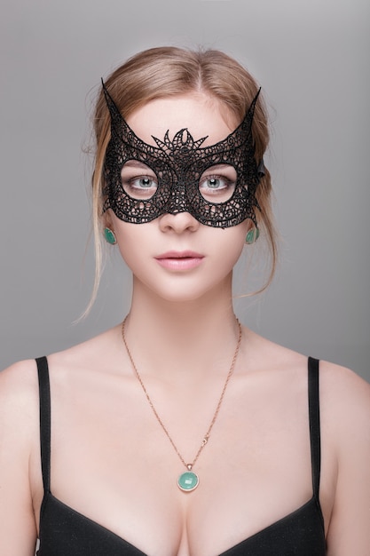 Ritratto di bella donna bionda sensuale con gli occhi verdi nella maschera di pizzo nero su uno sfondo scuro. maschera veneziana