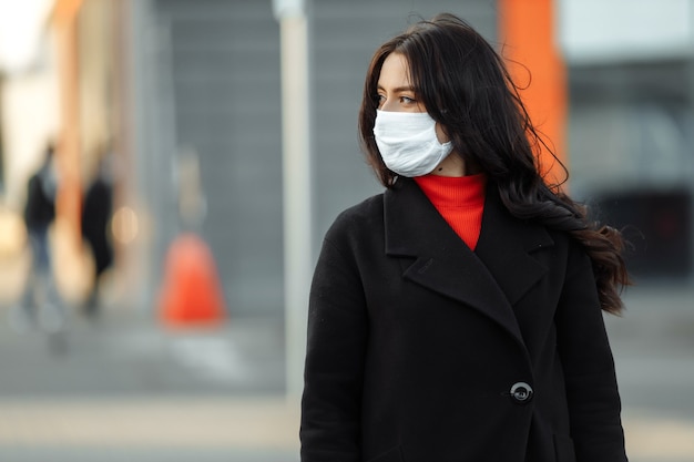 Ritratto di bella donna che cammina per strada indossando maschera protettiva come protezione contro