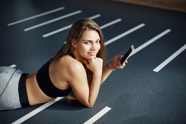 Ritratto di bella donna che risiede in palestra dopo un duro allenamento utilizzando uno smart phone per pubblicare foto sui social media.