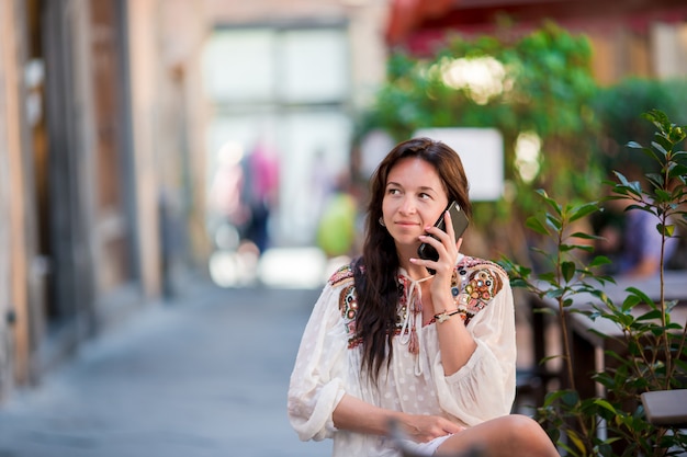 Ritratto di bella donna che si siede nel caffè all'aperto bevendo caffè e parlando da smartphone.