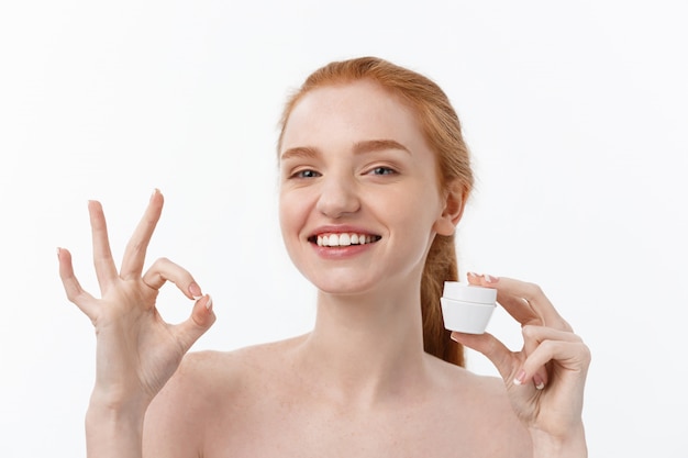 Ritratto di bella donna che sorride mentre prendendo una certa crema facciale isolata su bianco