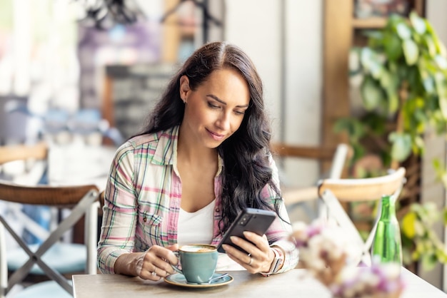 Ritratto di bella donna che usa il suo smarphone nella caffetteria che legge i messaggi ricevuti