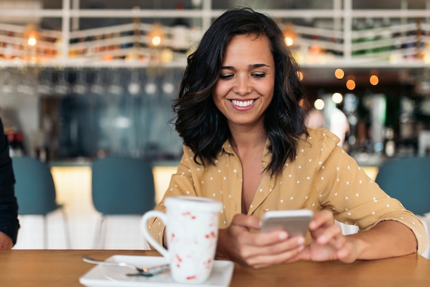 Ritratto di bella donna che utilizza cellulare nella caffetteria.