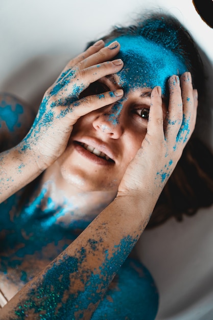 Ritratto di bella donna con scintillii blu sul viso nella vasca da bagno. Il concetto di individualità