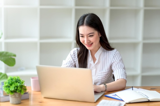 Ritratto di bella donna d'affari asiatica sorridente godetevi l'idea seduta con il computer portatile in ufficio