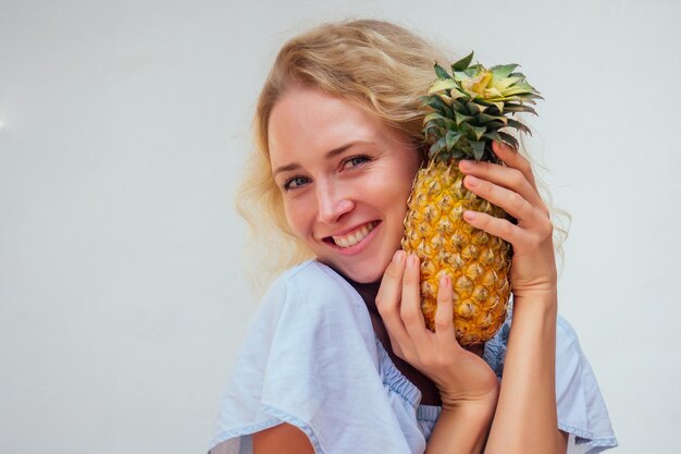 Ritratto di bella donna dai capelli biondi con gli occhi azzurri che tiene l'ananas su sfondo biancodetox e allergia ai prodotti tropicali