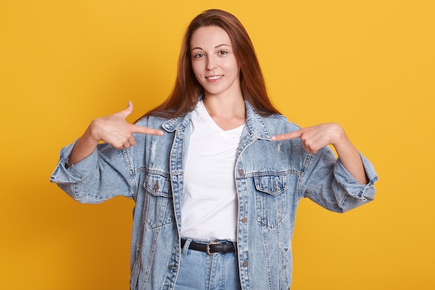 Ritratto di bella donna in giacca di jeans, sta indicando se stessa con entrambe le mani