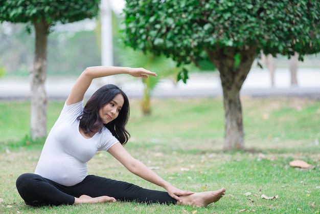 Ritratto di bella donna incinta asiatica al parcoThailandia personeFelice concetto di donnaIl suo gioco di yoga sul prato