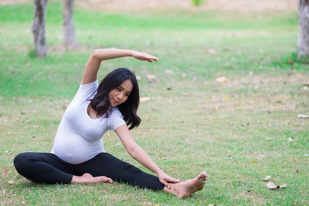 Ritratto di bella donna incinta asiatica al parcoThailandia personeFelice concetto di donnaIl suo gioco di yoga sul prato