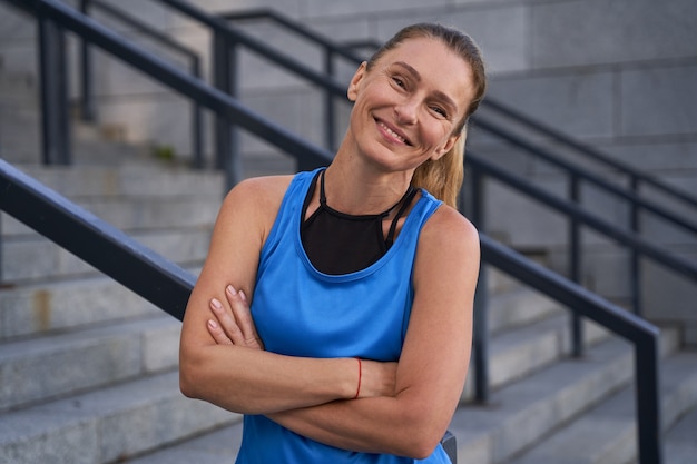 Ritratto di bella donna matura sportiva in abiti sportivi che sorride alla telecamera in piedi con le braccia incrociate