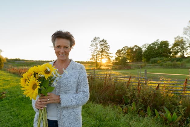 Ritratto di bella donna scandinava matura nel campo di girasoli in fiore all'aperto