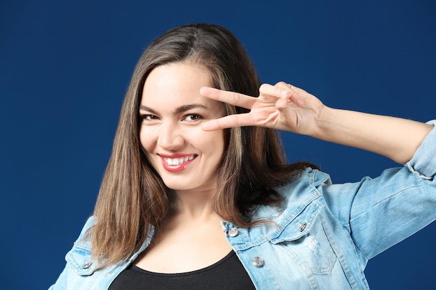 Ritratto di bella donna sorridente che mostra gesto di vittoria su sfondo colorato