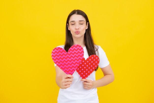 Ritratto di bella donna sorridente che tiene il cuore di carta nelle sue mani su sfondo giallo Amore concetto Amore segno simboli per felice giorno di San Valentino o compleanno delle donne