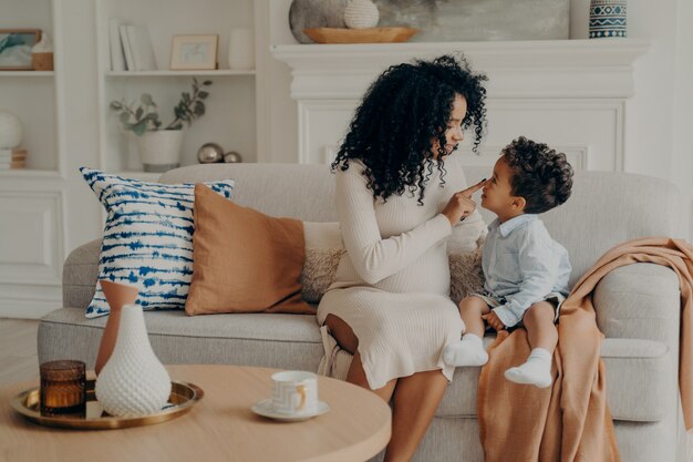 Ritratto di bella famiglia incinta madre e figlio di razza afro etnica seduta sul divano