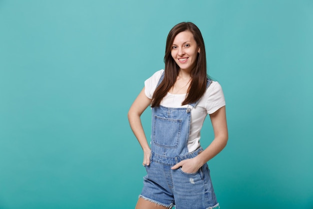 Ritratto di bella giovane donna abbastanza sorridente in vestiti casuali del denim che stanno isolata sul fondo blu della parete del turchese in studio. Persone sincere emozioni, concetto di stile di vita. Mock up spazio copia.