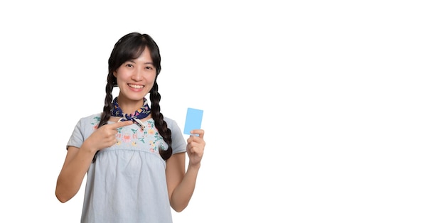 Ritratto di bella giovane donna asiatica felice in vestito dal denim che tiene carta di credito su fondo bianco