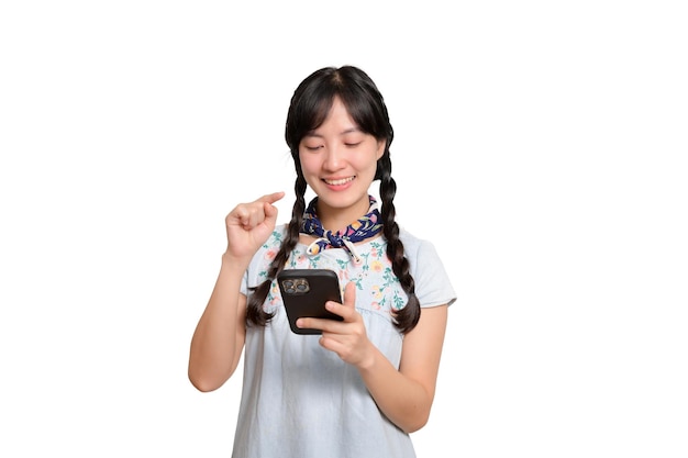 Ritratto di bella giovane donna asiatica felice in vestito dal denim facendo uso di uno smartphone sul colpo bianco dello studio del fondo