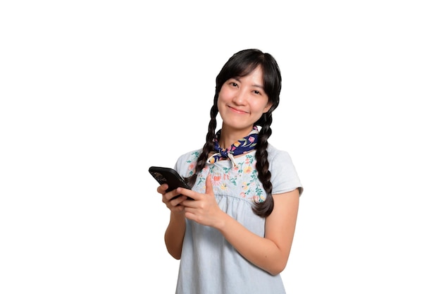 Ritratto di bella giovane donna asiatica felice in vestito dal denim facendo uso di uno smartphone sul colpo bianco dello studio del fondo