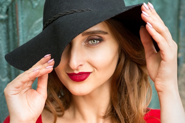 Ritratto di bella giovane donna caucasica alla moda in vestito rosso che porta il cappello nero