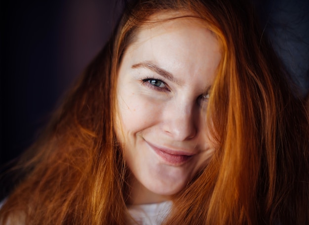 Ritratto di bella giovane donna con capelli rossi spessi e arruffati, primo piano. Bellezza dagli occhi grigi che guarda l'obbiettivo e sorridente. Pubblicità di prodotti per la cura della pelle o dei capelli.