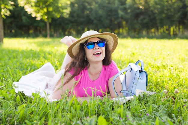 Ritratto di bella giovane donna con cappello e occhiali da sole sdraiato nel parco durante un picnic