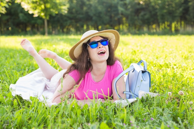 Ritratto di bella giovane donna con cappello e occhiali da sole sdraiato nel parco durante un picnic