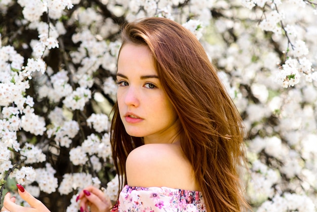 Ritratto di bella giovane donna dai capelli rossi in abito bianco in fiori primaverili