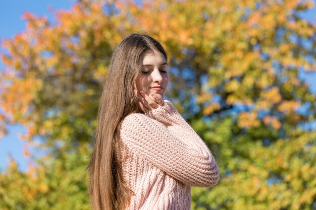 Ritratto di bella giovane donna in elegante maglione lavorato a maglia in piedi sulla foresta autunnale dorata in una giornata di sole