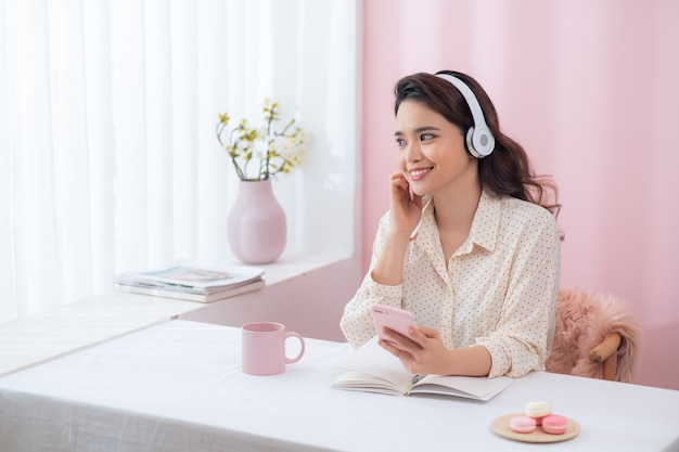 Ritratto di bella giovane donna sorridente felice seduta in ufficio, ascoltando musica in cuffia