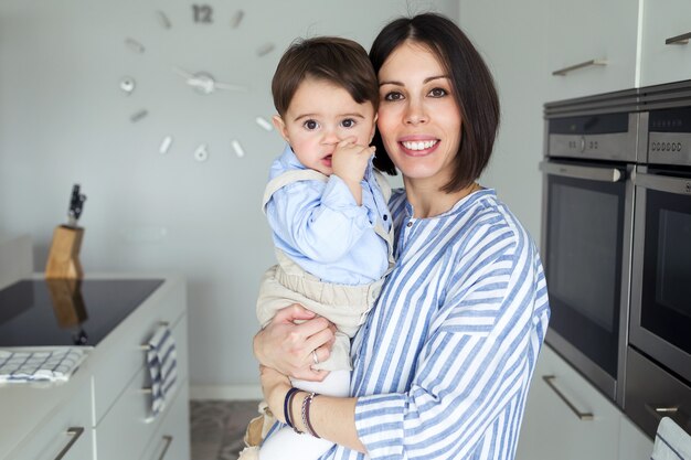 Ritratto di bella madre con il suo bambino che guarda l'obbiettivo in cucina a casa.