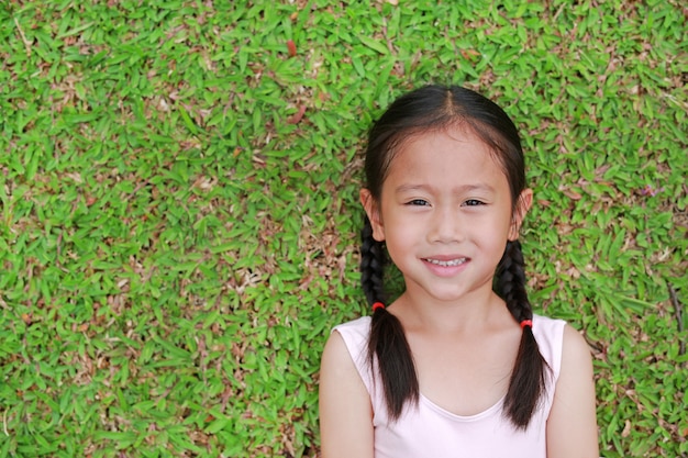 Ritratto di bella piccola ragazza asiatica del bambino con due capelli della coda di cavallo che si trovano sul prato inglese dell'erba verde.
