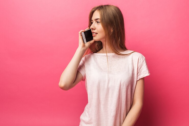 Ritratto di bella ragazza allegra che parla sul telefono, distogliendo lo sguardo, abbastanza divertente, isolato sulla parete rosa, pubblicità