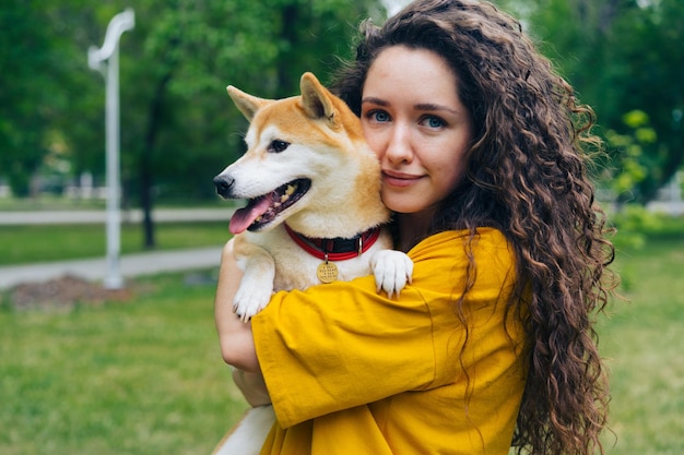 Ritratto di bella ragazza amorevole proprietario del cane in piedi nel parco con il suo bellissimo animale domestico sorridente