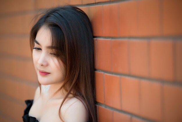 Ritratto di bella ragazza asiatica chic indossare abito nero posa per scattare una foto sul muro di mattoni Stile di vita della gente della Tailandia teenager Concetto felice della donna moderna