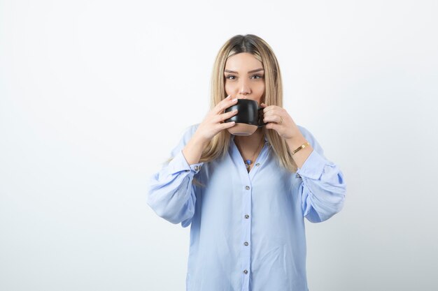 Ritratto di bella ragazza che beve il caffè al mattino contro il muro bianco