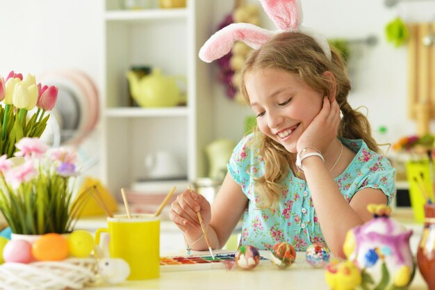 Ritratto di bella ragazza in orecchie da coniglio che dipingono le uova per le vacanze di Pasqua