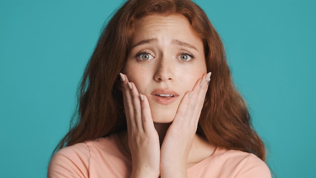 Ritratto di bella ragazza rossa timida che guarda colpevolmente a porte chiuse su sfondo colorato