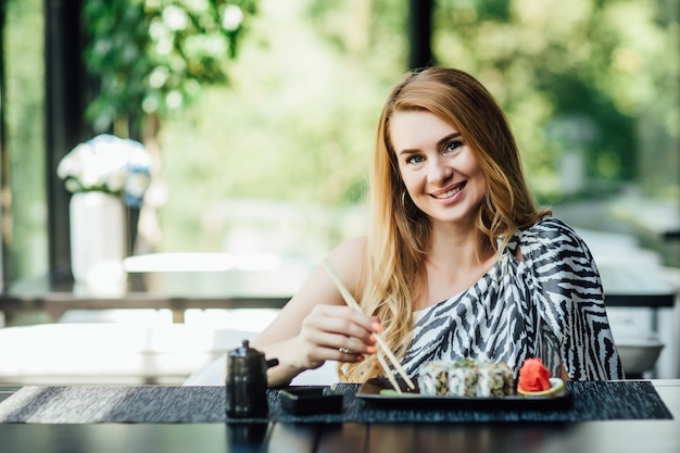 Ritratto di bella signora di mezza età si siede nella caffetteria sulla terrazza estiva con set di rotoli di sushi.