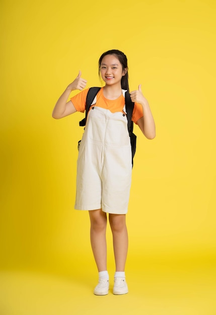 ritratto di bella studentessa asiatica che indossa uno zaino su uno sfondo gialloxA