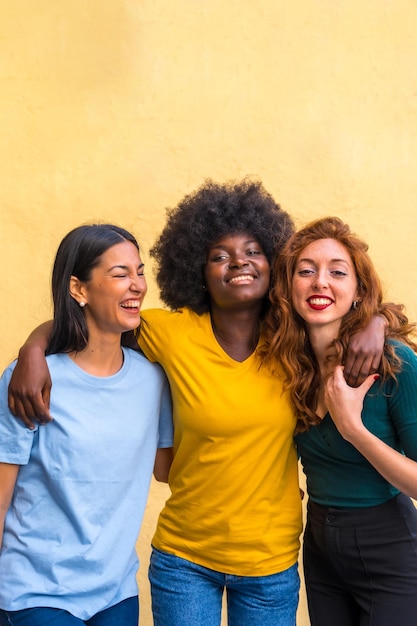 Ritratto di belle amiche multietniche che sorridono su una parete gialla divertendosi copia incolla