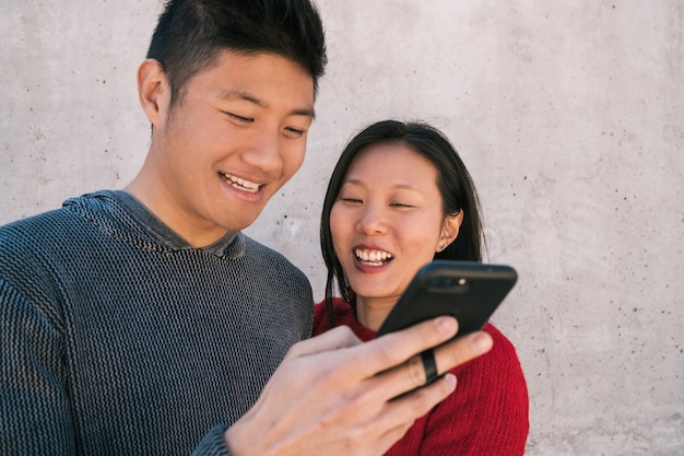 Ritratto di belle coppie asiatiche guardando il telefono cellulare mentre trascorrono del buon tempo insieme. Amore e concetto di tecnologia.