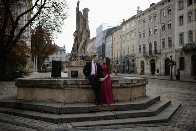 Ritratto di belle coppie sorridenti di amore che si siedono vicino alla fontana all'aperto nella città.