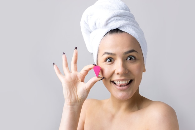 Ritratto di bellezza della donna in asciugamano bianco sulla testa con una spugna per un corpo in vista di un cuore rosa. Cura della pelle pulizia eco cosmetici biologici spa relax concetto.